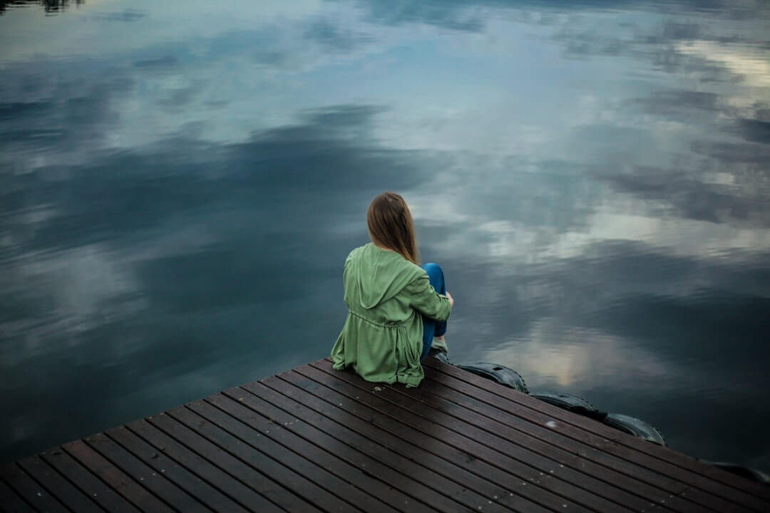 A woman sitting alone on a couch looking at her phone, waiting for a reply