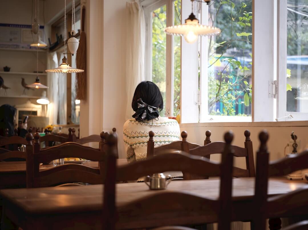 woman sitting alone by a window looking thoughtful, soft afternoon light