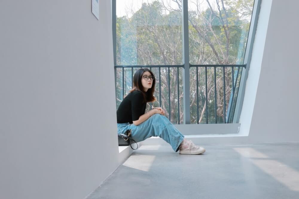 Woman sitting alone at a window, looking thoughtfully at her phone in soft natural light