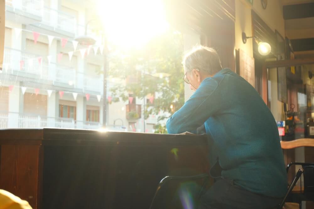 person sitting alone at a cafe table looking thoughtful, window light